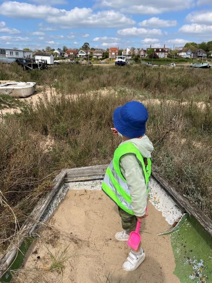 Child in sand boat looking at marsh